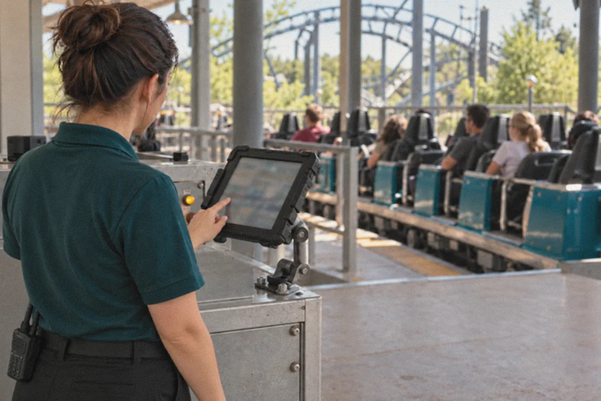 Ride operator using RideOps on a tablet mounted at the station control panel while guests sit in the coaster train